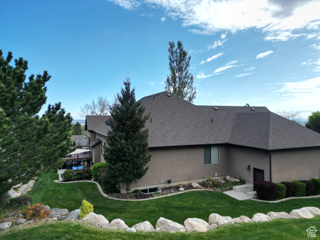 View of side of property featuring roof with shingles, stucco siding, and a lawn