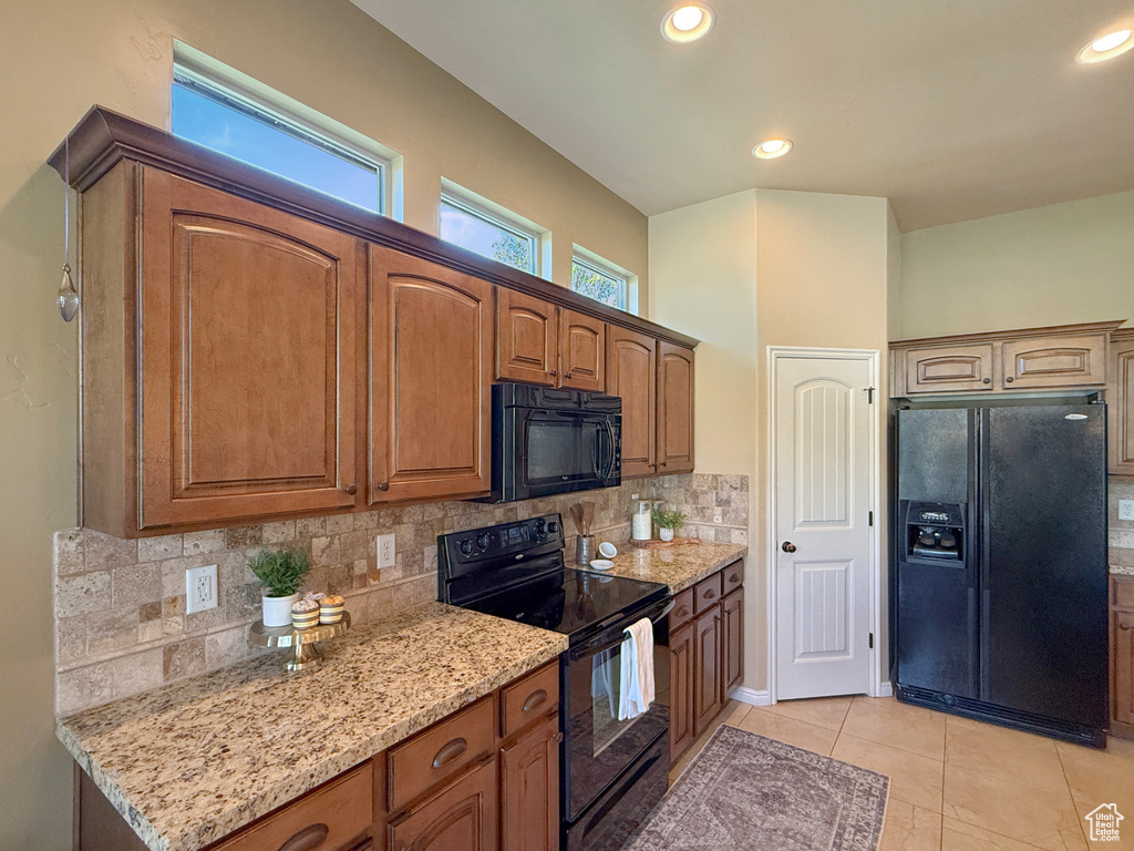 Kitchen with light tile patterned flooring, light stone counters, brown cabinetry, backsplash, and black appliances