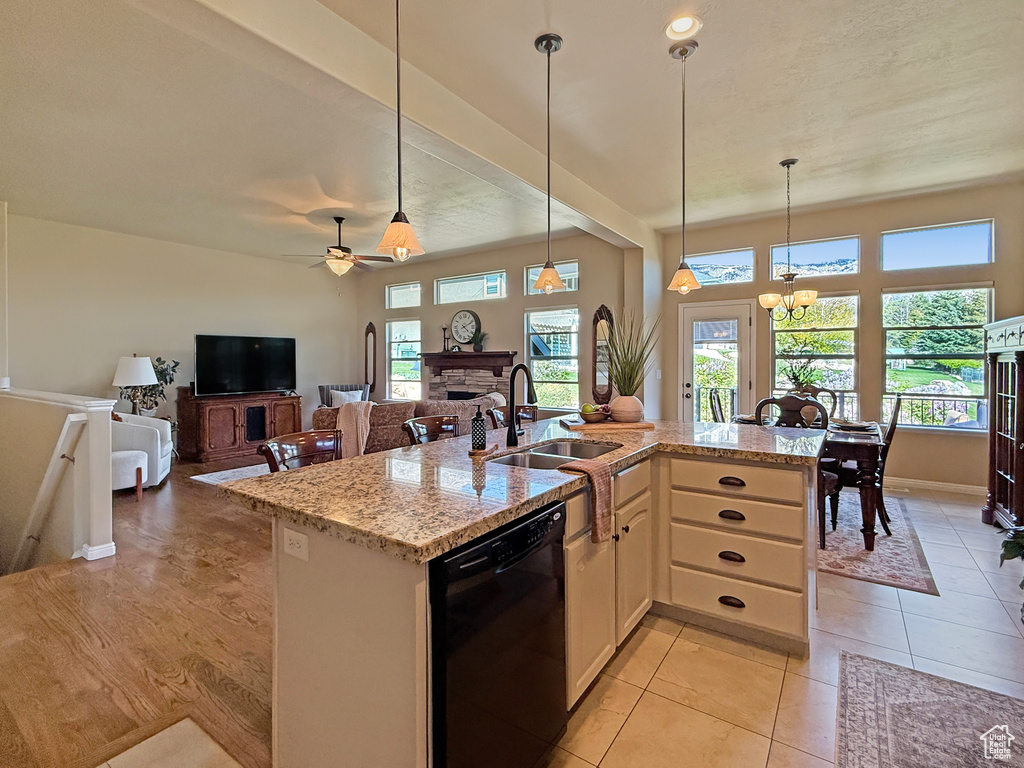 Kitchen featuring black dishwasher, light stone countertops, decorative light fixtures, and a sink