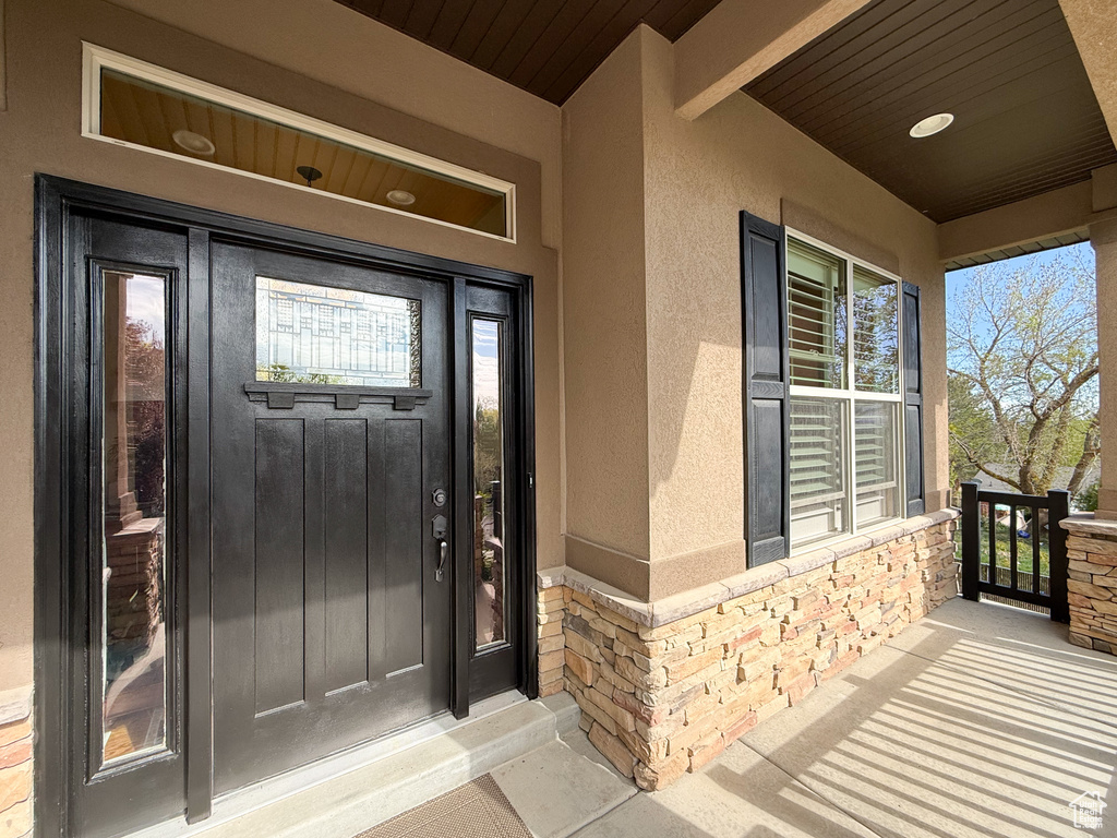 Entrance to property featuring a porch, stone siding, and stucco siding