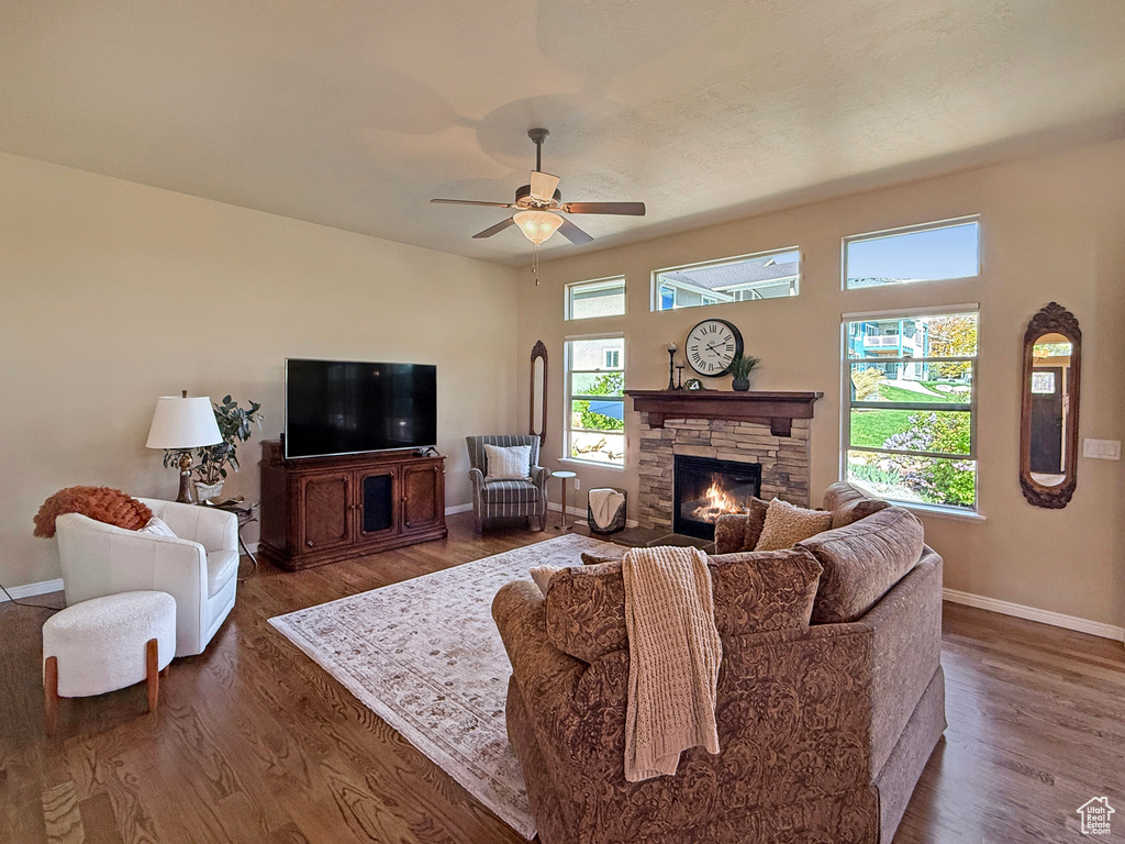 Living room featuring baseboards, a ceiling fan, wood finished floors, and a stone fireplace