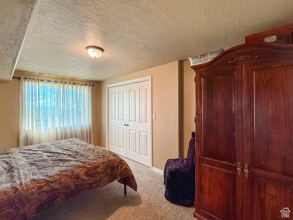Carpeted bedroom featuring a textured ceiling, baseboards, and a closet