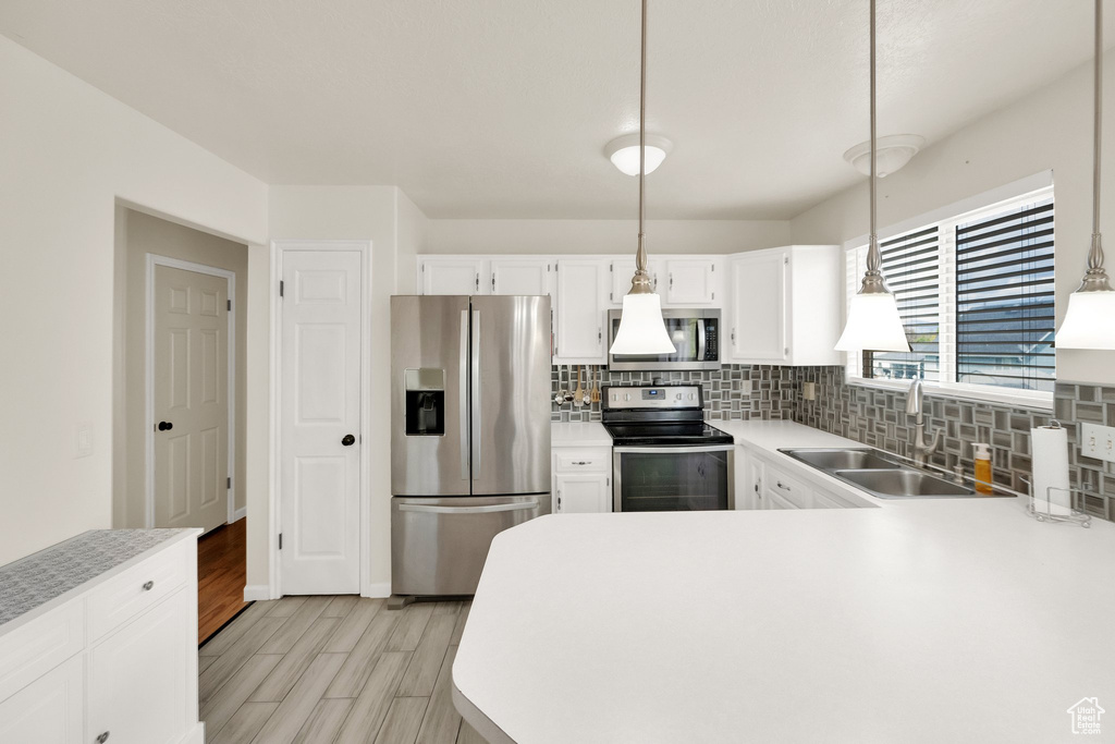 Kitchen with light countertops, tasteful backsplash, a sink, light wood finished floors, and appliances with stainless steel finishes