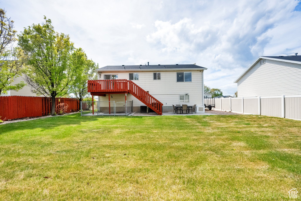 Back of property with stairs, a wooden deck, a fenced backyard, a patio, and a yard