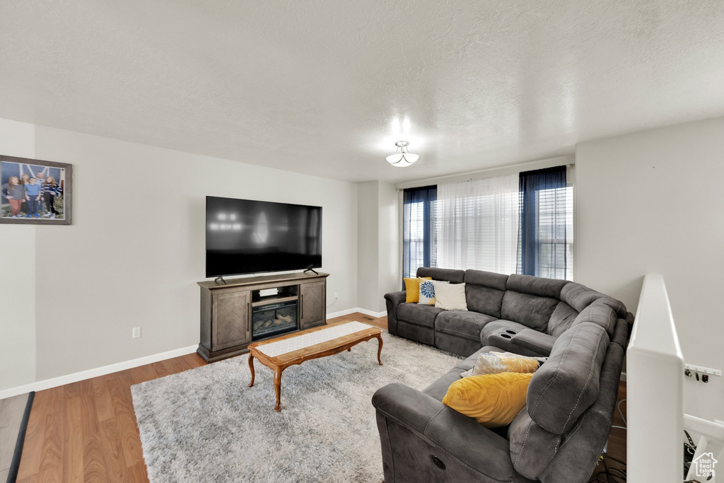 Living room featuring a glass covered fireplace, baseboards, a textured ceiling, and wood finished floors