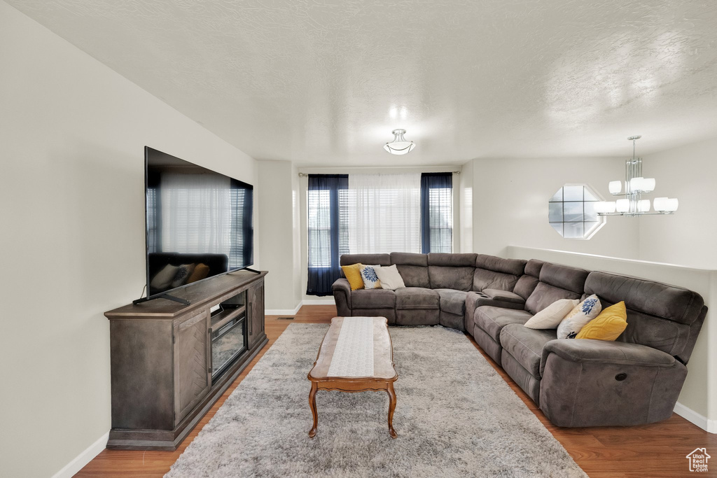 Living room featuring an inviting chandelier, baseboards, a textured ceiling, and wood finished floors