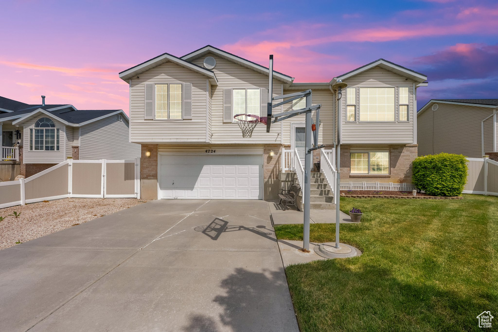 Raised ranch featuring concrete driveway, fence, a front yard, and a garage