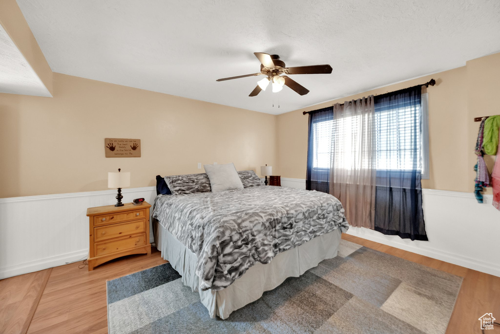 Bedroom with a ceiling fan, wainscoting, and light wood finished floors