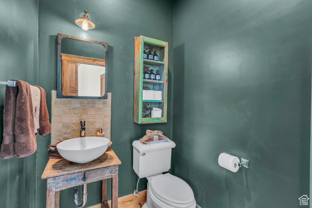 Half bathroom featuring a sink, toilet, baseboards, decorative backsplash, and wood finished floors