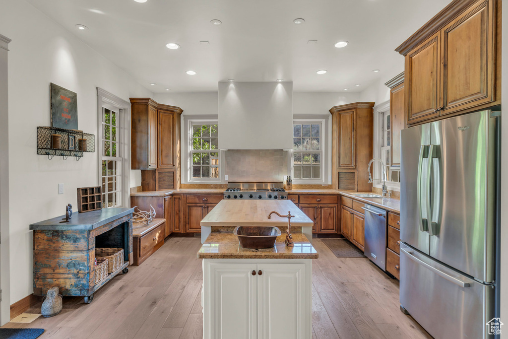 Kitchen featuring brown cabinets, appliances with stainless steel finishes, range hood, and a center island