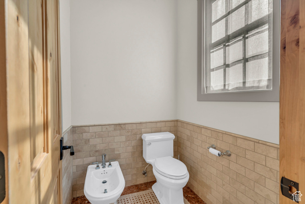 Half bath featuring wainscoting, toilet, tile walls, tile patterned floors, and a bidet
