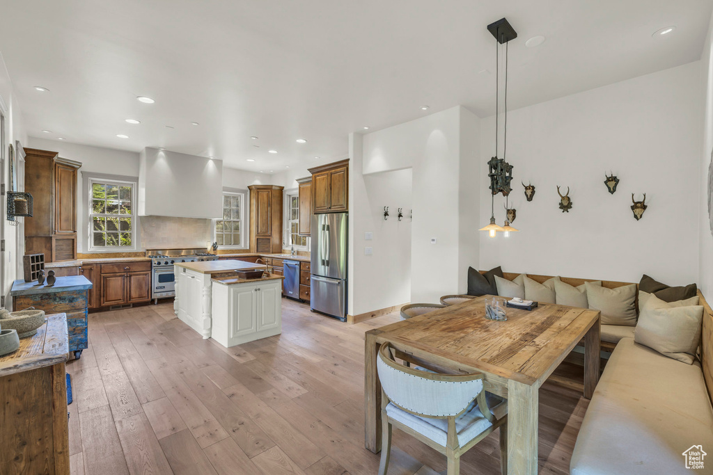 Kitchen featuring wall chimney range hood, brown cabinetry, appliances with stainless steel finishes, a center island, and light wood finished floors