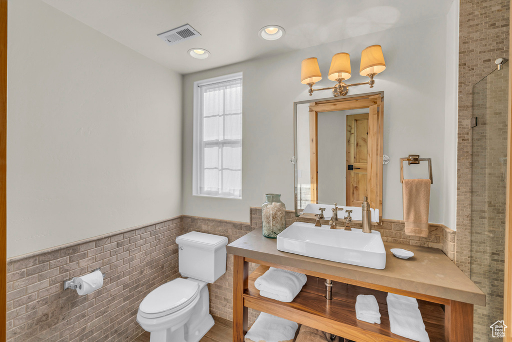 Bathroom featuring visible vents, tile walls, a wainscoted wall, vanity, and toilet