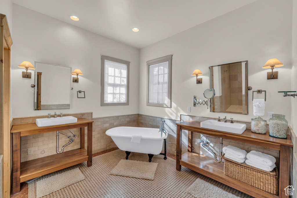 Full bath featuring a sink, wainscoting, tile walls, and a soaking tub