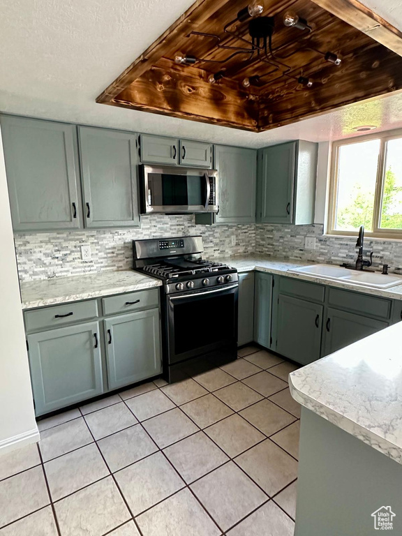 Kitchen featuring a sink, decorative backsplash, stainless steel appliances, and light tile patterned flooring