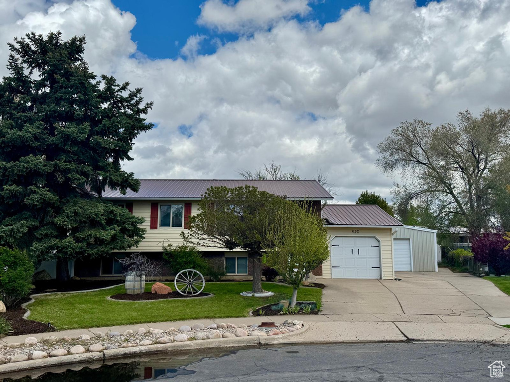 View of front of property featuring concrete driveway, an attached garage, metal roof, and a front yard