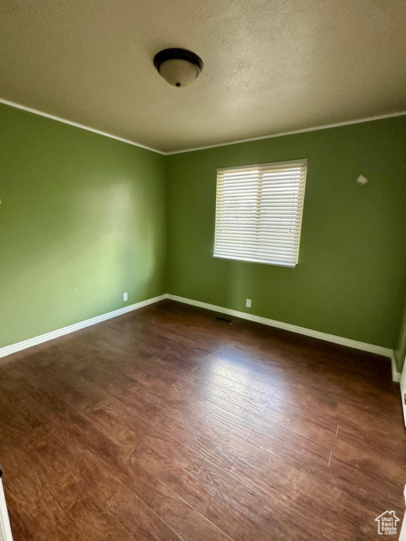 Spare room with baseboards, a textured ceiling, and dark wood-style floors