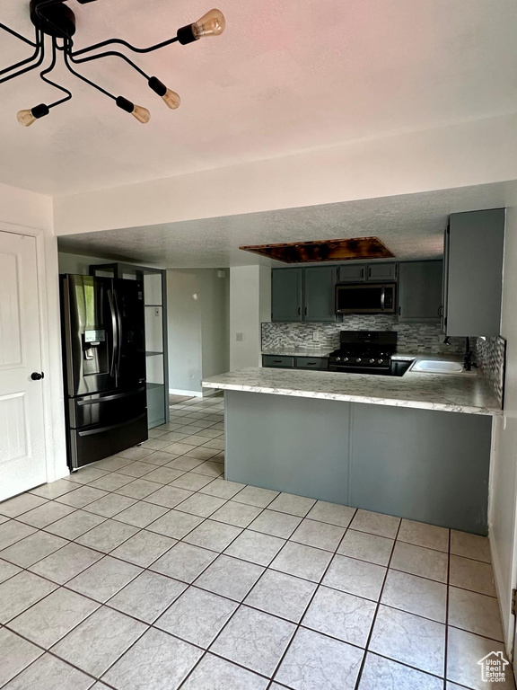 Kitchen with light countertops, tasteful backsplash, a sink, light tile patterned floors, and black appliances