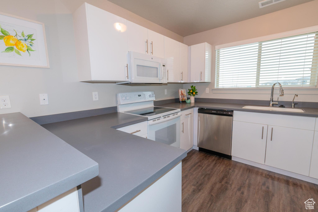 Kitchen with white appliances, white cabinets, a sink, and dark wood-type flooring