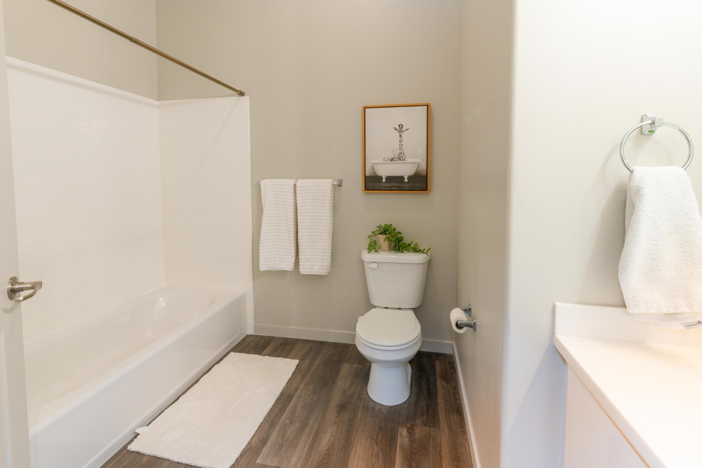 Full bathroom featuring vanity, wood finished floors, toilet, baseboards, and  shower combination