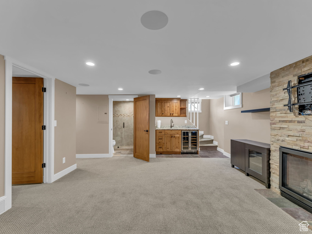 Unfurnished living room featuring wine cooler, baseboards, wet bar, and light colored carpet