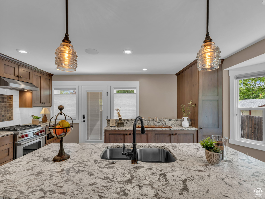 Kitchen with light stone countertops, under cabinet range hood, tasteful backsplash, a sink, and high end stainless steel range oven