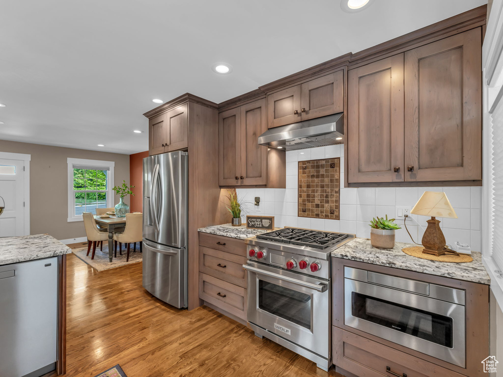 Kitchen featuring appliances with stainless steel finishes, tasteful backsplash, light wood-style floors, under cabinet range hood, and recessed lighting
