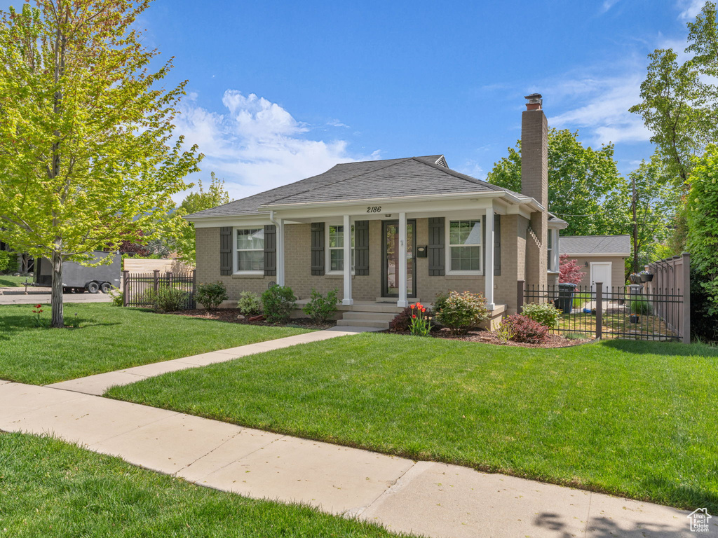 Bungalow with fence, a chimney, a front lawn, and brick siding