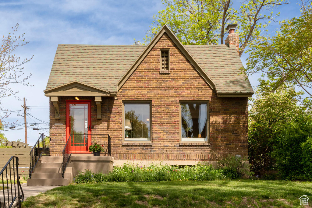 View of front of home featuring a shingled roof, a chimney, a front lawn, and brick siding