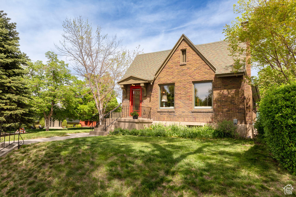 English style home with roof with shingles, a front yard, and brick siding