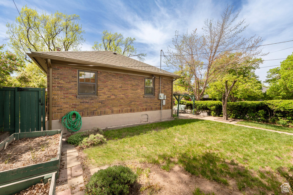 View of home's exterior featuring a gate, brick siding, fence, a yard, and a shingled roof