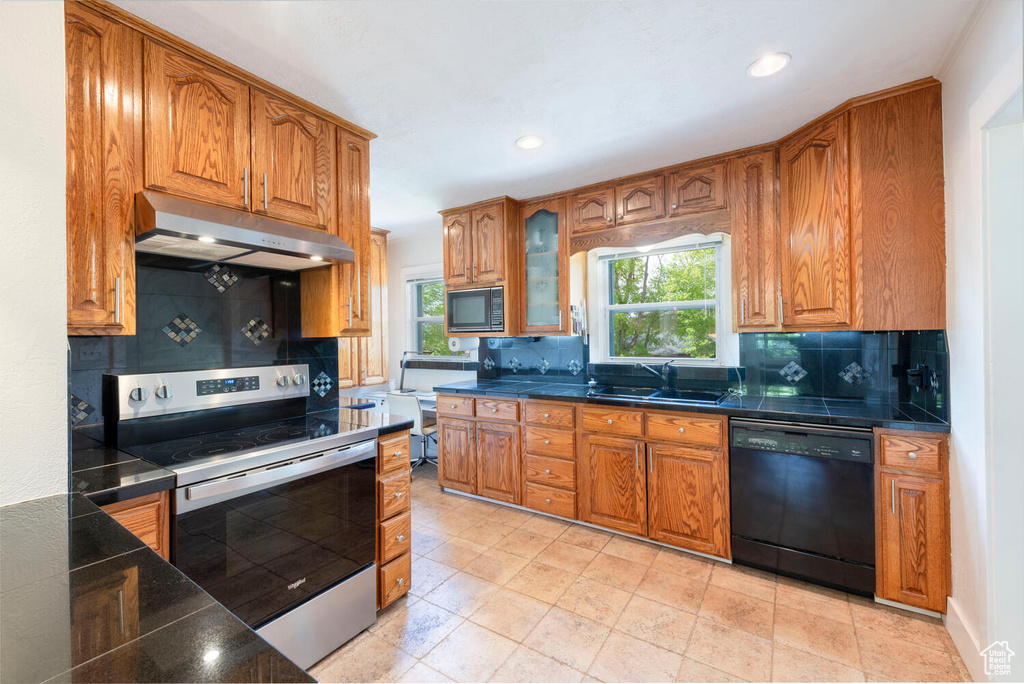 Kitchen featuring black appliances, plenty of natural light, under cabinet range hood, and a sink