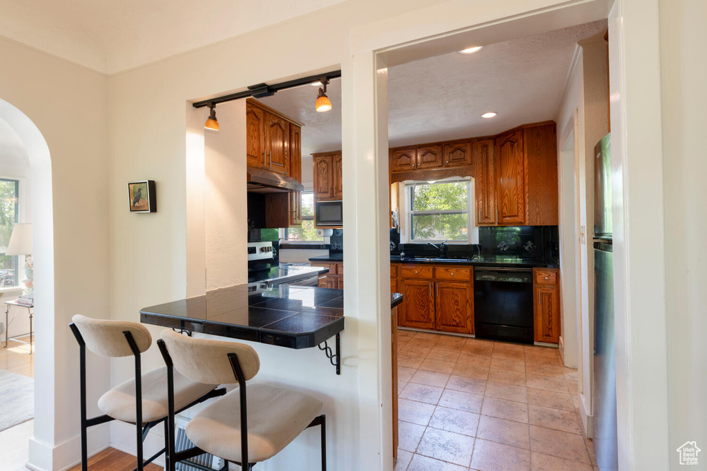 Kitchen featuring brown cabinets, a sink, a breakfast bar area, under cabinet range hood, and black appliances