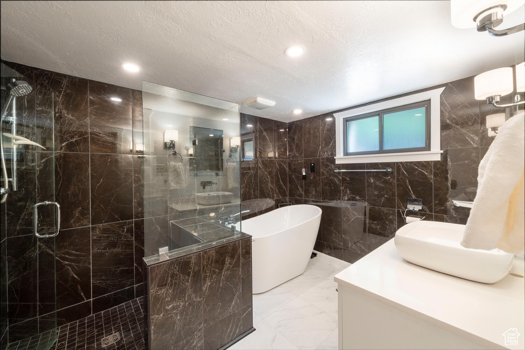 Bathroom with marble finish floor, a stall shower, a freestanding tub, and tile walls