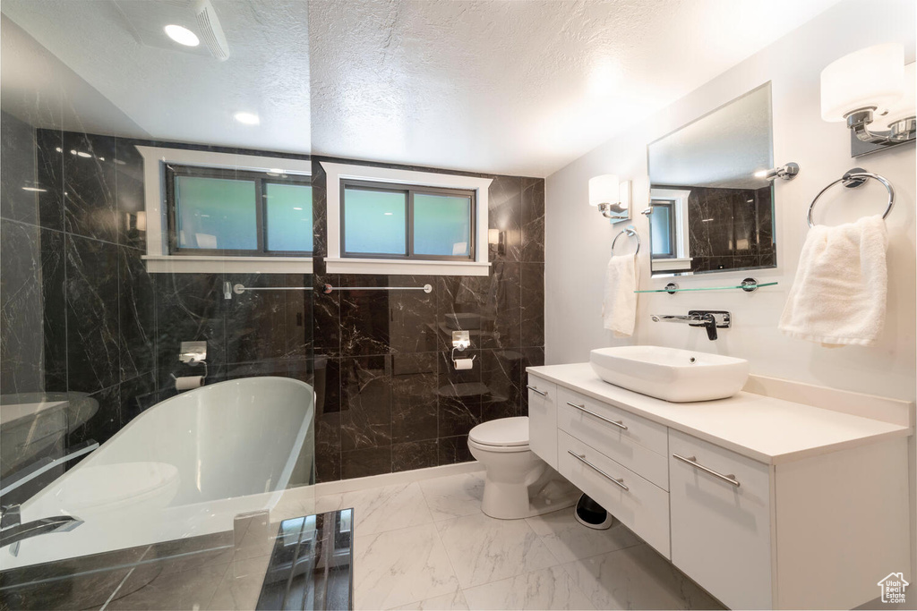 Bathroom featuring a textured ceiling, a freestanding tub, vanity, toilet, and marble finish floor