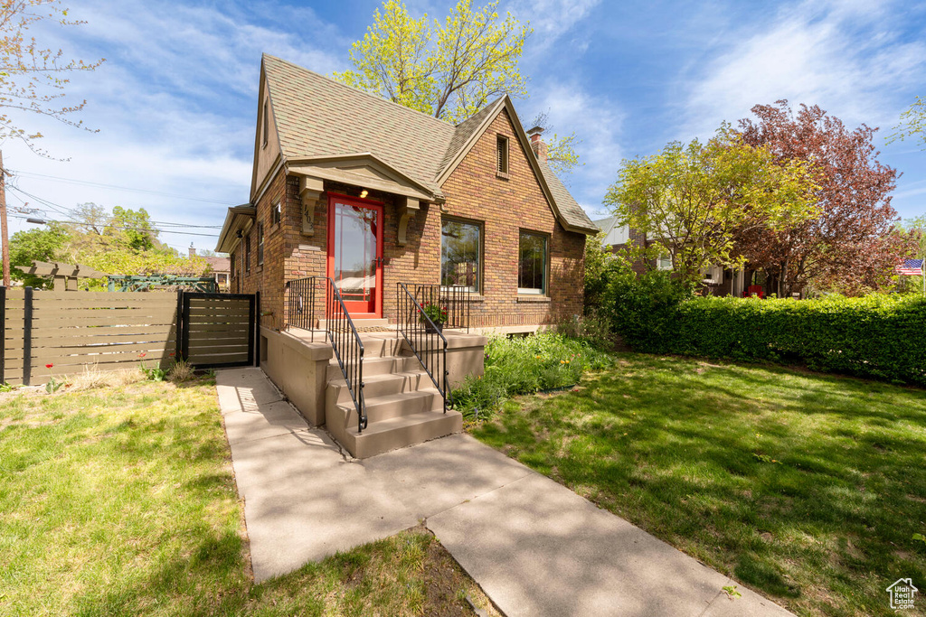 View of front of home featuring brick siding, fence, a shingled roof, and a front lawn