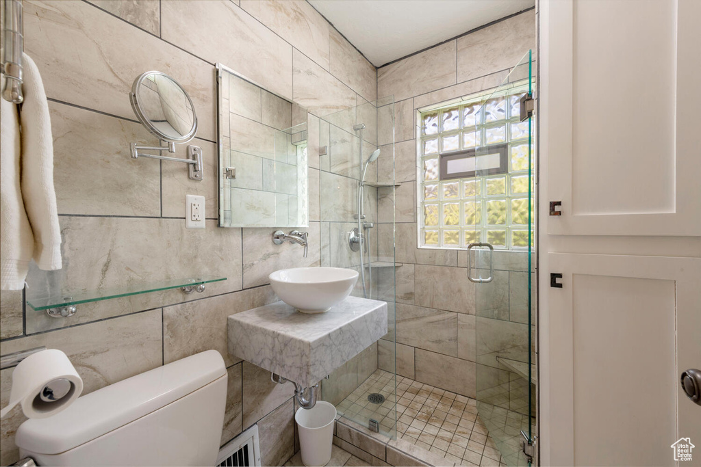 Bathroom featuring a sink, tile walls, a shower stall, and toilet
