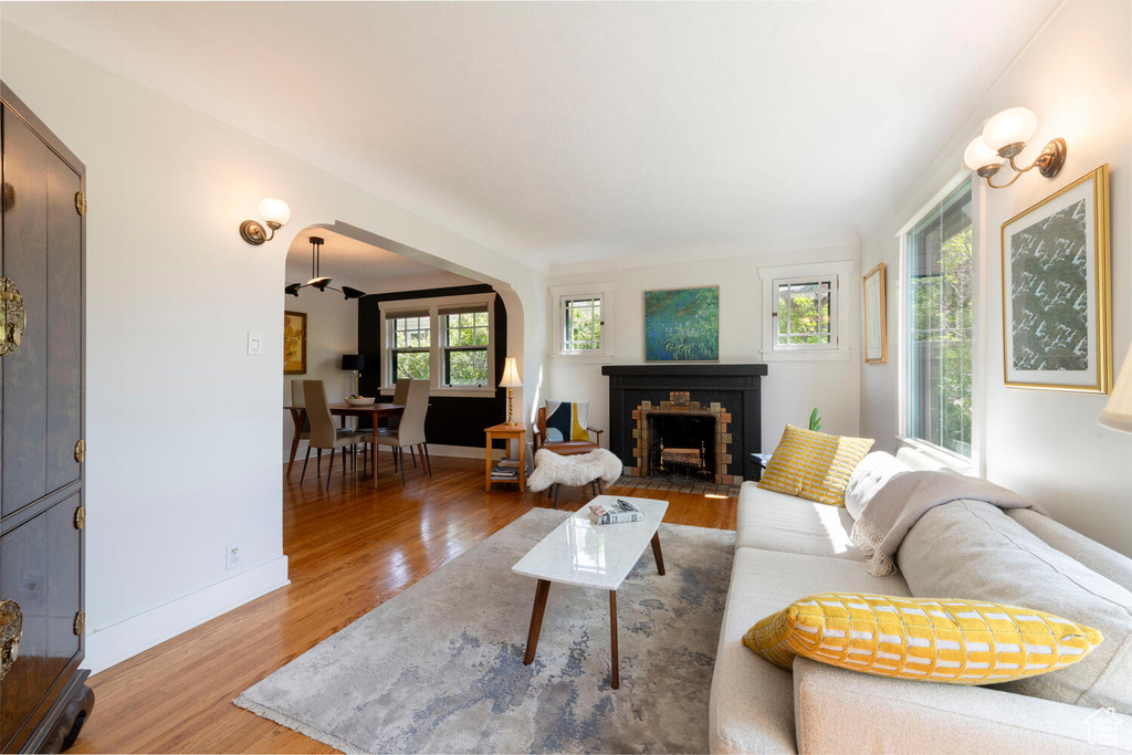 Living room featuring a brick fireplace, arched walkways, baseboards, and wood finished floors