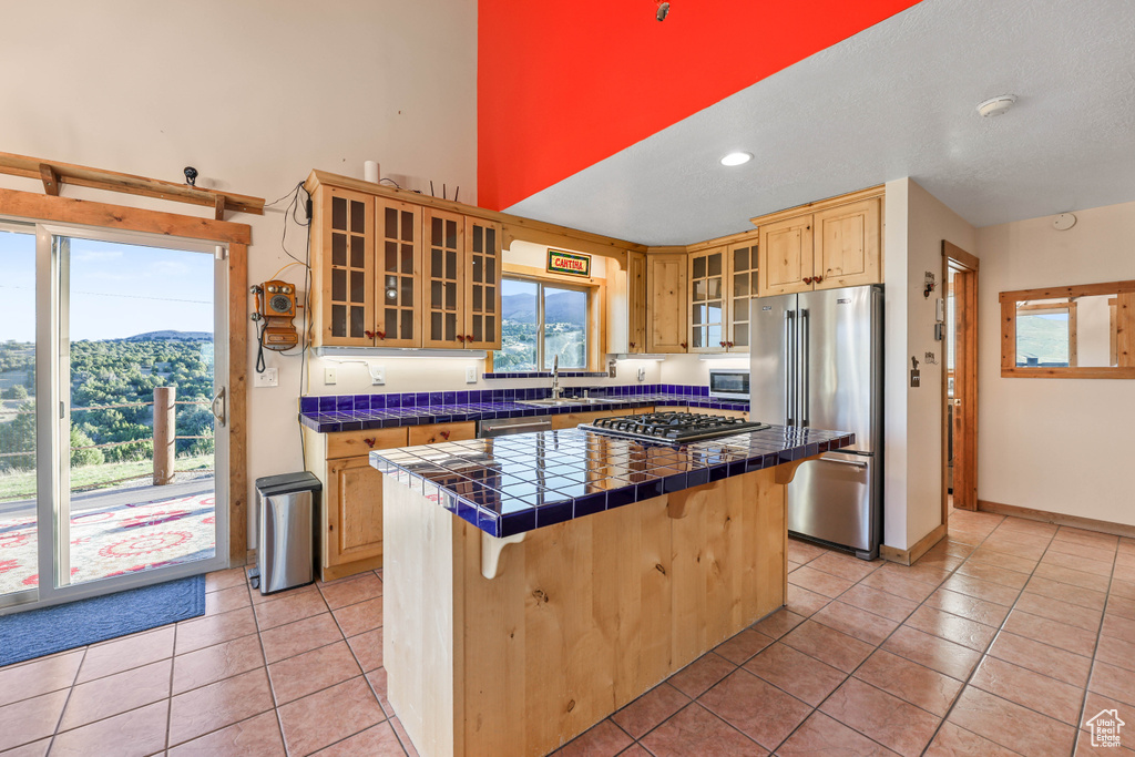 Kitchen with light tile patterned flooring, a breakfast bar, tile counters, stainless steel appliances, and a kitchen island