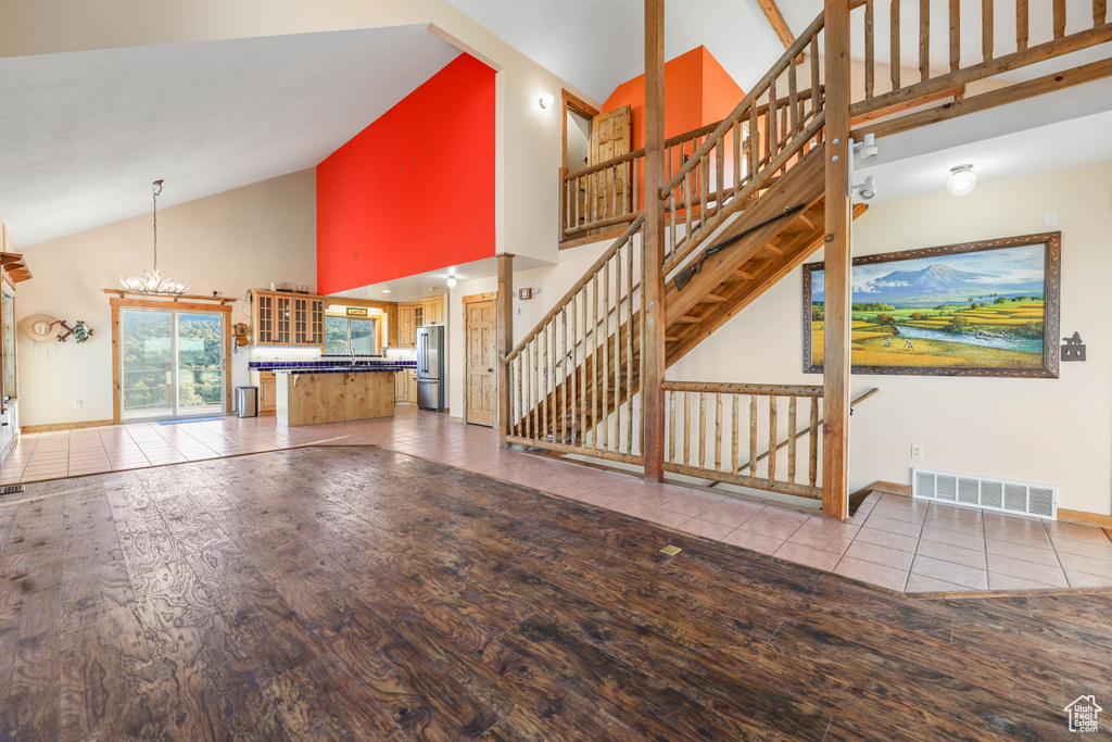 Unfurnished living room with an inviting chandelier, high vaulted ceiling, wood finished floors, visible vents, and stairway