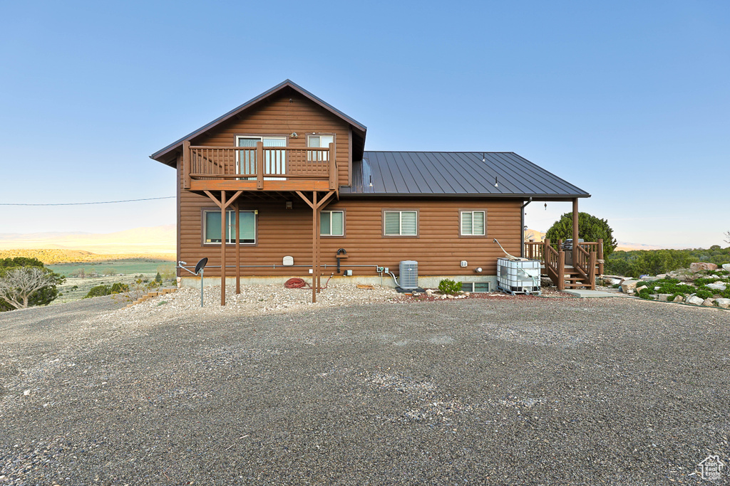 Back of house with gravel driveway, central AC, and metal roof