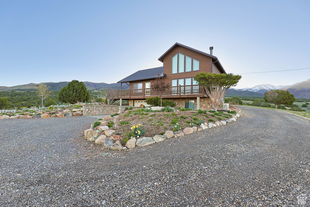 View of front of property featuring a deck with mountain view, driveway, and metal roof