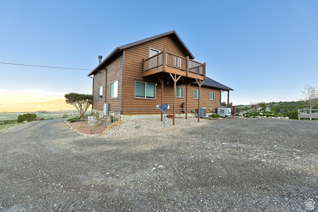 Back of property with faux log siding, a balcony, gravel driveway, and cooling unit