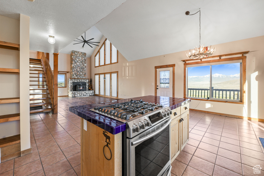 Kitchen featuring stainless steel range with gas stovetop, tile counters, a stone fireplace, and light tile patterned floors