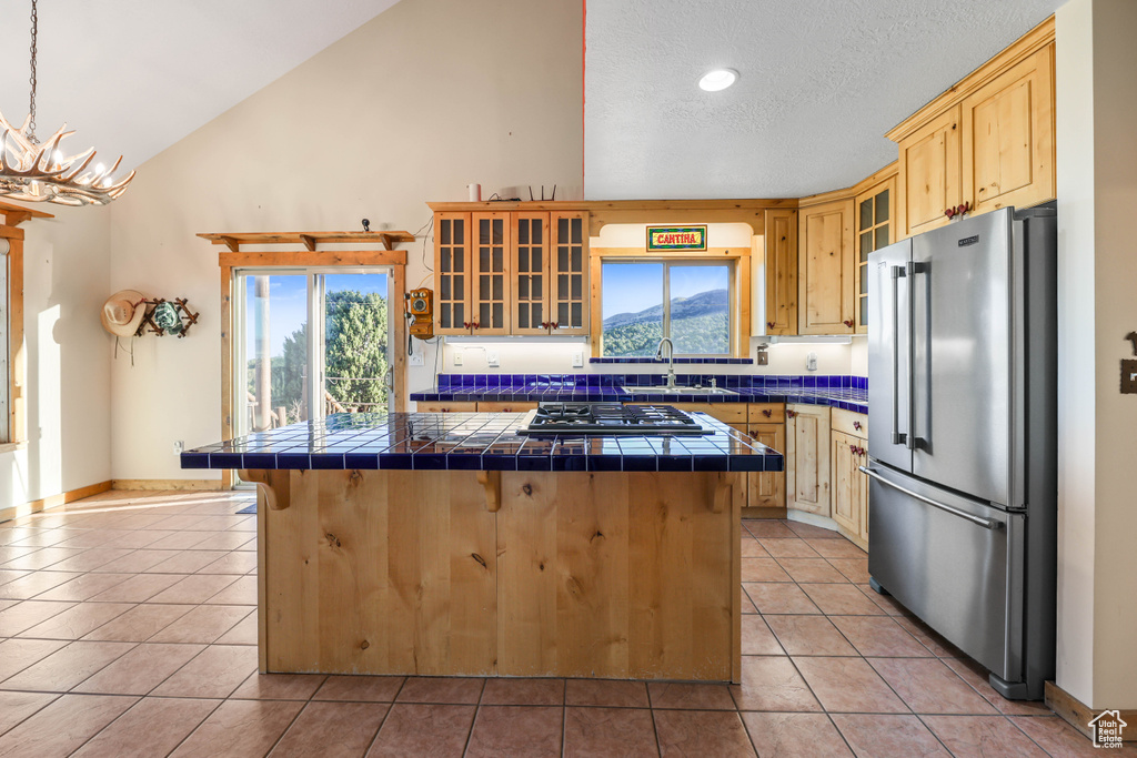 Kitchen with a kitchen island, appliances with stainless steel finishes, a sink, tile counters, and light tile patterned flooring
