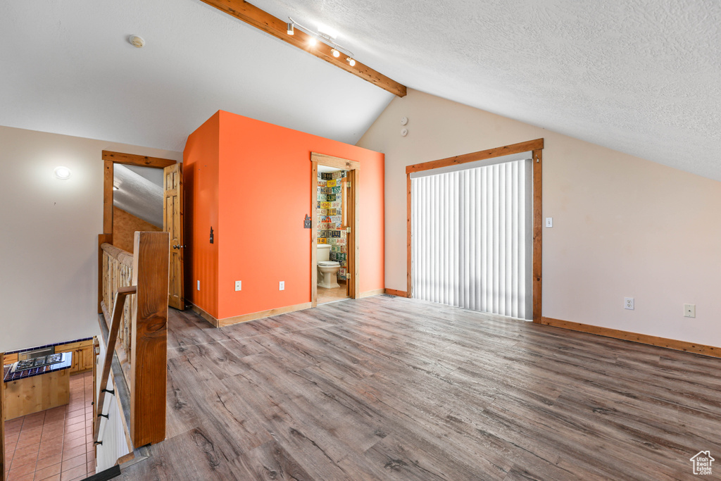 Additional living space with baseboards, vaulted ceiling with beams, a textured ceiling, and wood finished floors