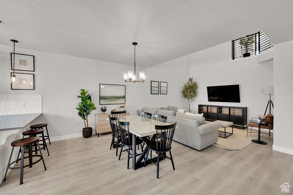 Dining area with a textured ceiling, baseboards, a chandelier, and light wood-type flooring