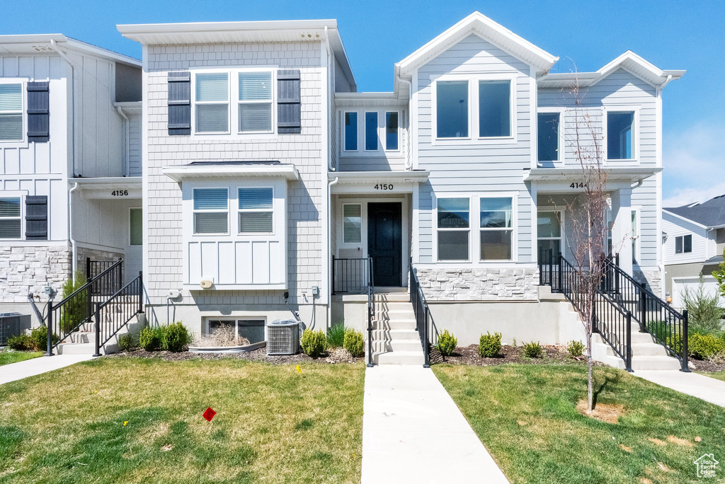 Townhome / multi-family property with stone siding, cooling unit, and a front yard