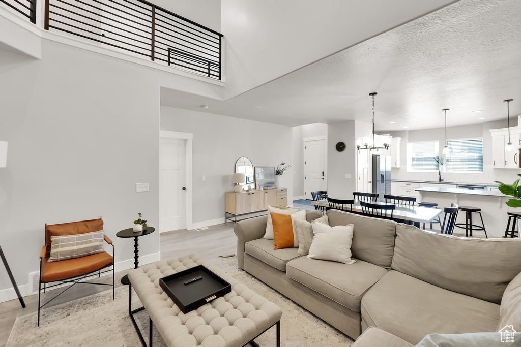 Living room with baseboards, light wood-style flooring, a high ceiling, and a chandelier