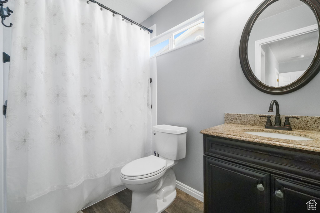 Bathroom featuring vanity, curtained shower, wood finished floors, toilet, and baseboards